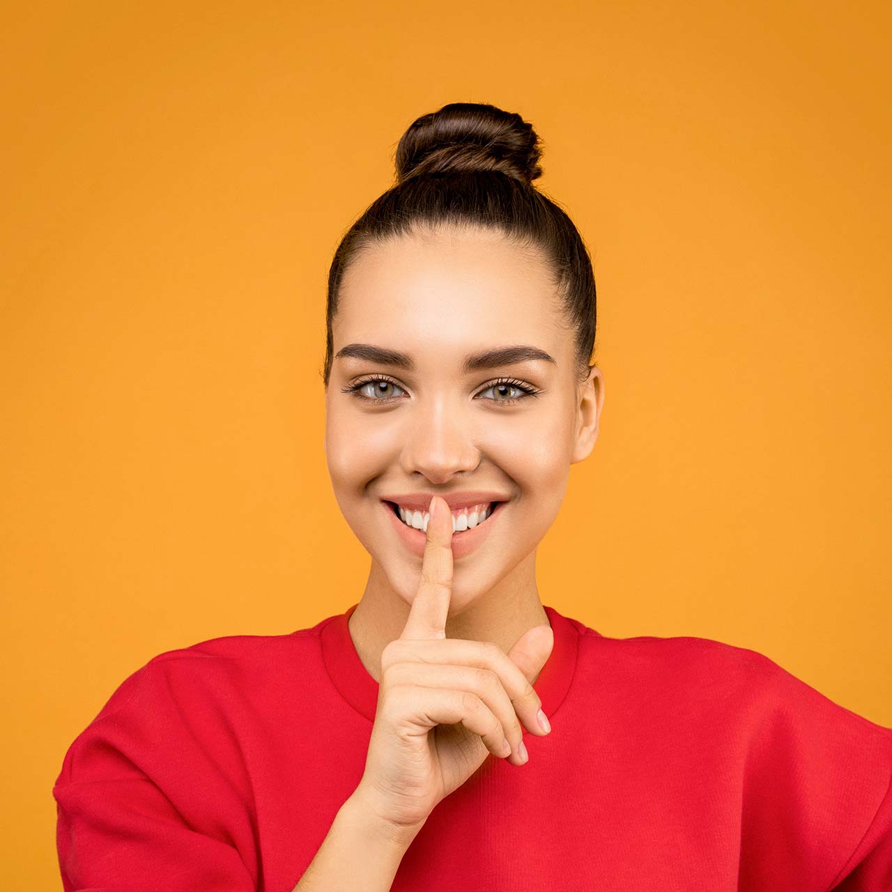 Photo of a smiling woman holding her index finger to her lips