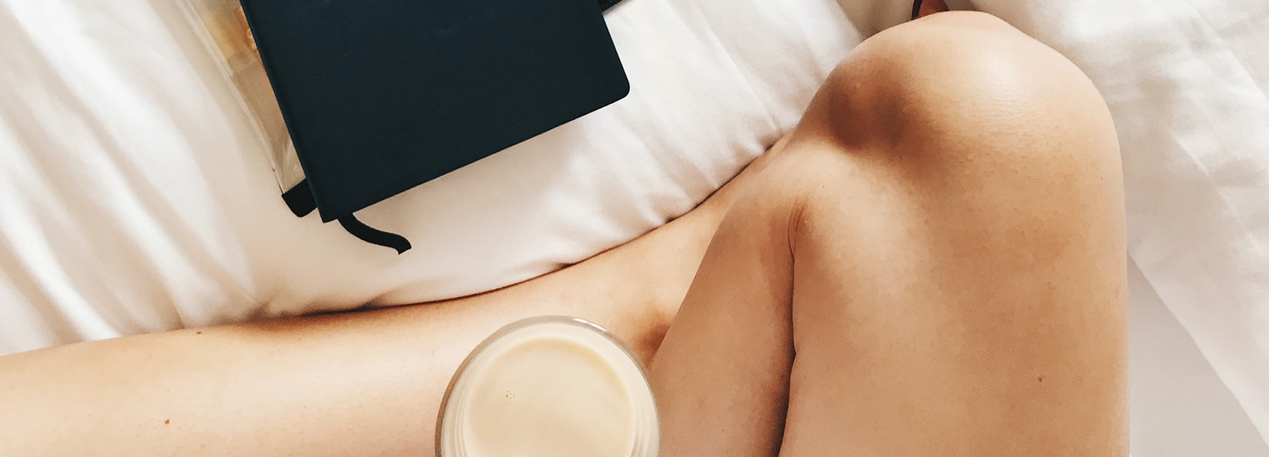 Detail of a woman sitting on her bed with a cup of coffee and a notebook or journal